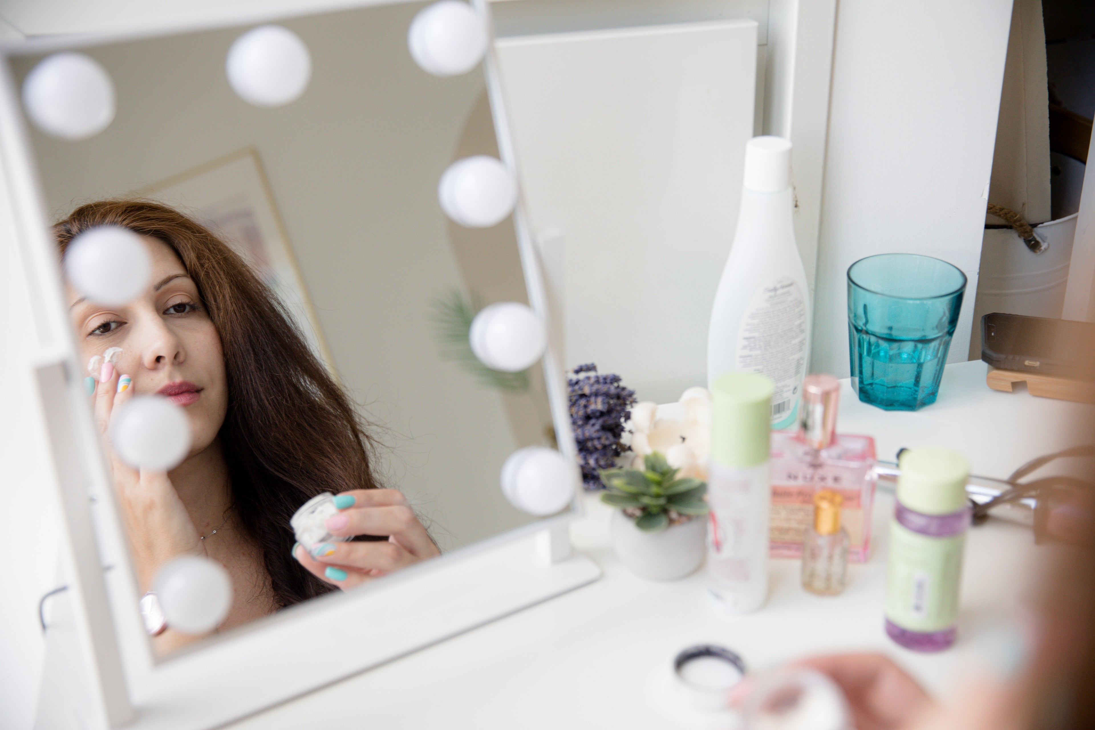 Image d'une jeune femme concentrée devant un miroir, appliquant soigneusement des produits de soin de la peau. Elle tient un flacon de sérum, symbole de sa routine beauté quotidienne. L'environnement est lumineux et épuré, mettant en valeur son engagement dans son rituel de soin personnel. Ce moment intime capte l'essence de la beauté quotidienne et l'importance de prendre soin de soi.